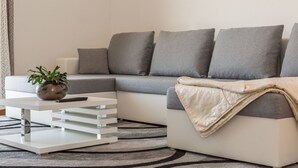 Un salon moderne avec un canapé d’angle gris, une table basse blanche et un tapis à motifs.