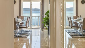 Un espace repas offrant une vue sur la mer, agrémenté d’une grande plante en pot et doté d’un aménagement intérieur moderne.