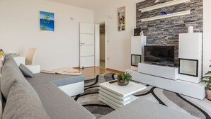 Un salon moderne avec un canapé gris, une table basse blanche et une cheminée dont la façade est en pierre.