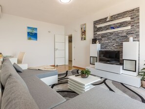 A modern living room with a grey sofa, a white coffee table, and a fireplace with a stone facade. - Große Wohnung in Omiš mit Möbliertem Balkon by Interhome (Omiš)