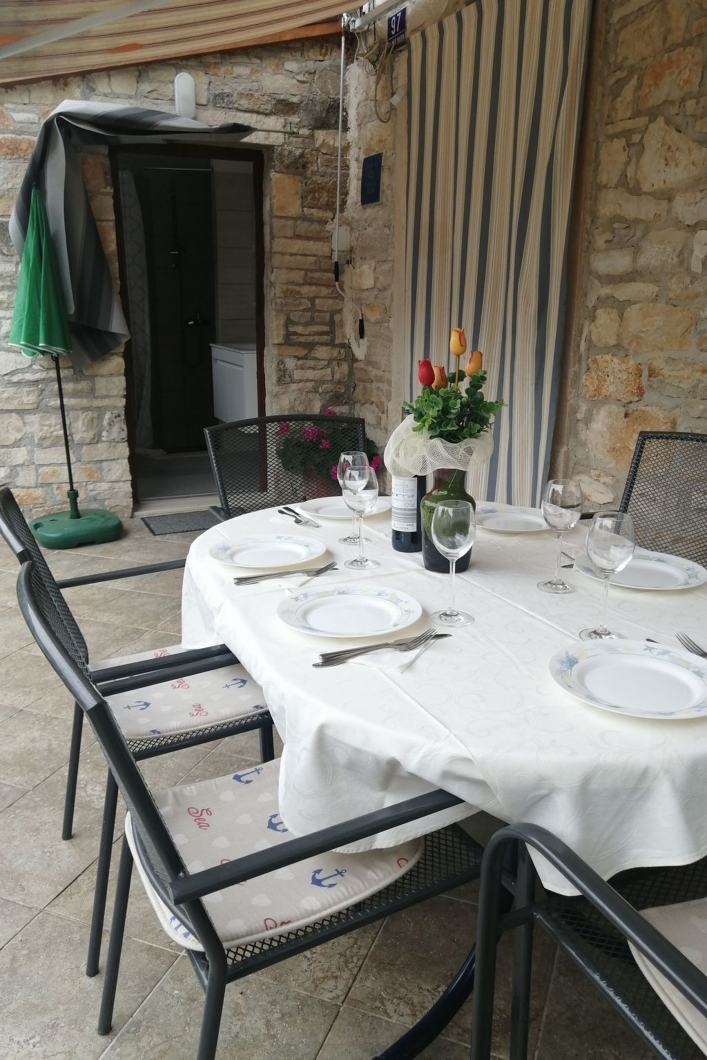 An outdoor dining area with a stone wall backdrop, a table set for four with white tablecloths and plates, and a vase with flowers.