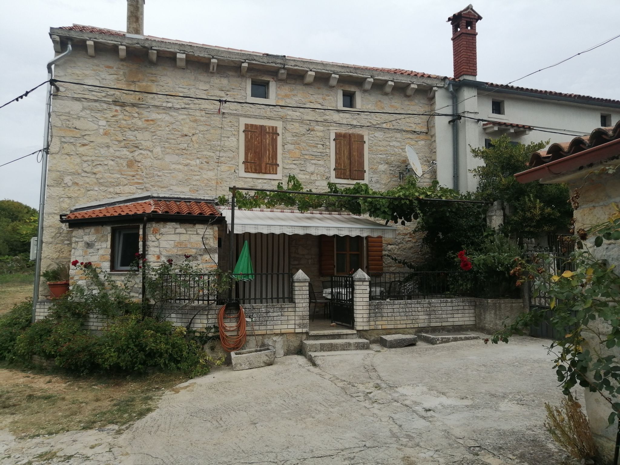 Ein Haus aus Stein mit einem Ziegeldach, einer kleinen Veranda und einem Garten.