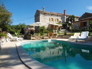 Uma vila de pedra com piscina, área de estar externa e vegetação exuberante.