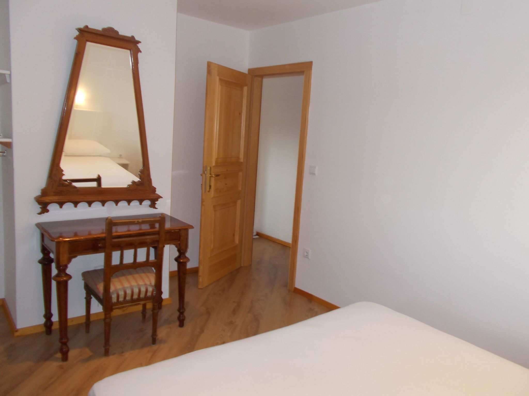 Un dormitorio con un aparador de madera, una silla, una cama y un espejo.