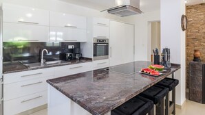 Una cocina moderna con gabinetes blancos, encimera de granito, horno empotrado y campana extractora de acero inoxidable.