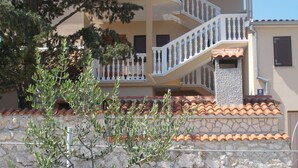 A multi-story building with a stone facade, a white balcony, and a tiled roof.