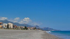 Una playa de guijarros con edificios y montañas al fondo.