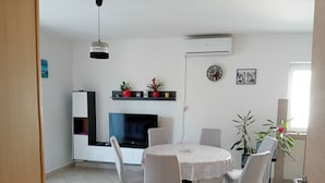 Un coin repas comprenant une table ronde, des chaises blanches, un téléviseur à écran plat et une petite étagère ornée d’objets décoratifs.