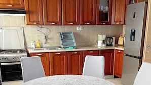 Une cuisine avec des meubles en bois, un réfrigérateur en acier inoxydable, une cuisinière et une table à manger avec des chaises blanches.