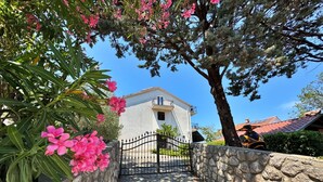 A stone pathway leading to a white building with a balcony, surrounded by greenery and pink flowers. - Apartment Lure by Interhome (Polje)