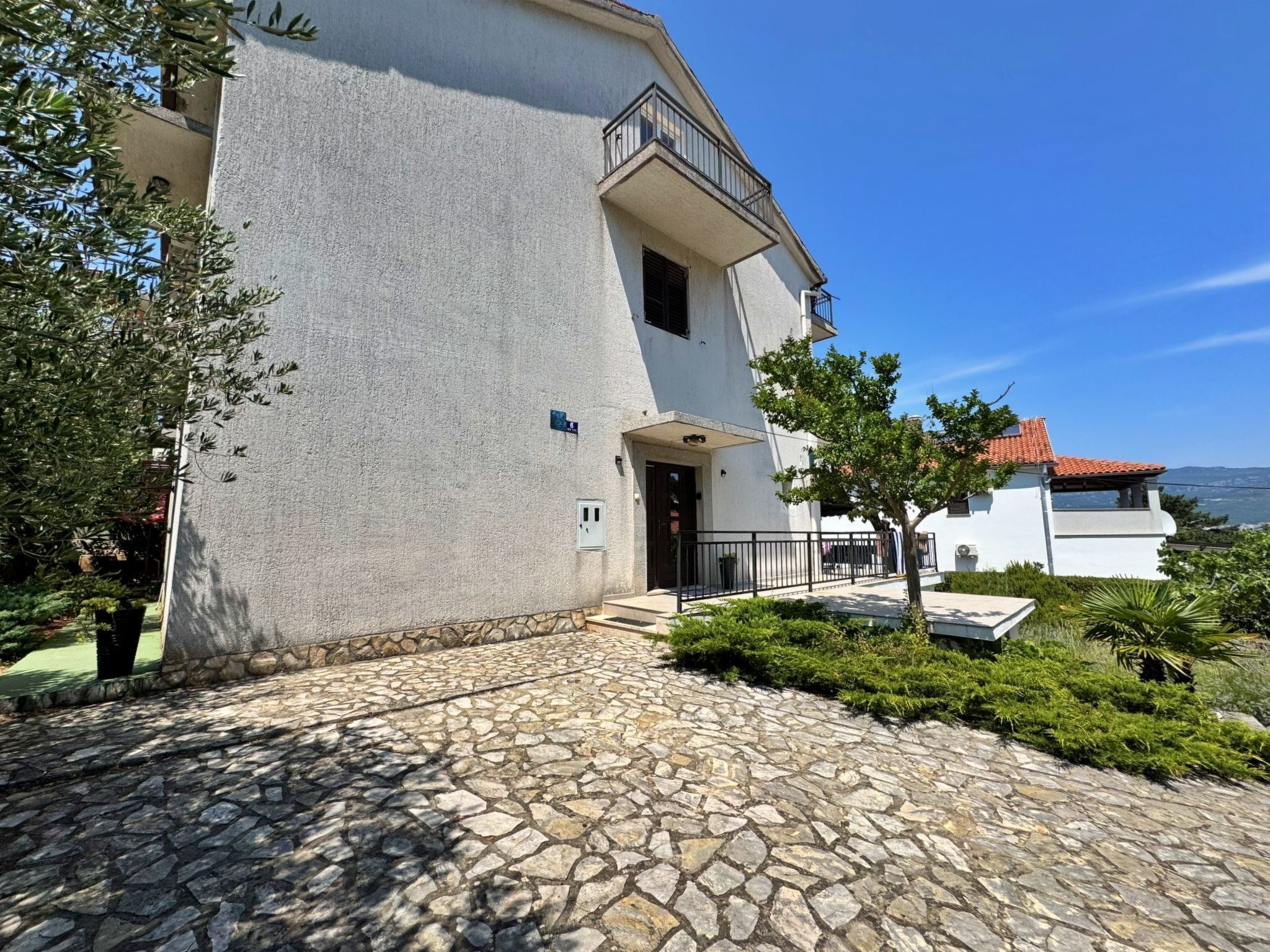 Um edifício com entrada de pedra, varanda e vista para o mar.