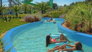 Una piscina con dos personas descansando en flotadores, rodeada de exuberante vegetación y un tobogán al fondo.