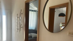 Um corredor com um aparador de madeira, um espelho redondo e uma porta que dá para um quarto.