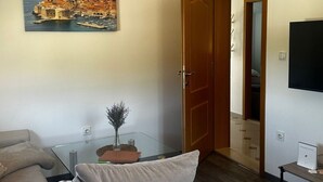 Uma sala de estar moderna com um sofá, uma pintura de uma cidade costeira, uma porta de madeira e uma TV na parede.