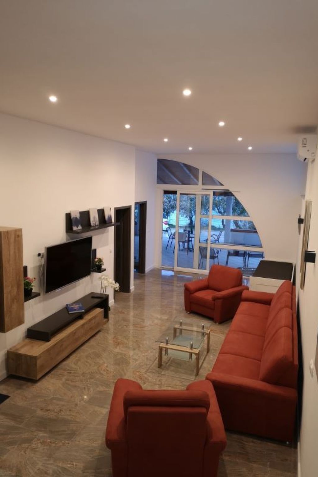 A modern living room with a large TV, red sofas, and a glass coffee table.