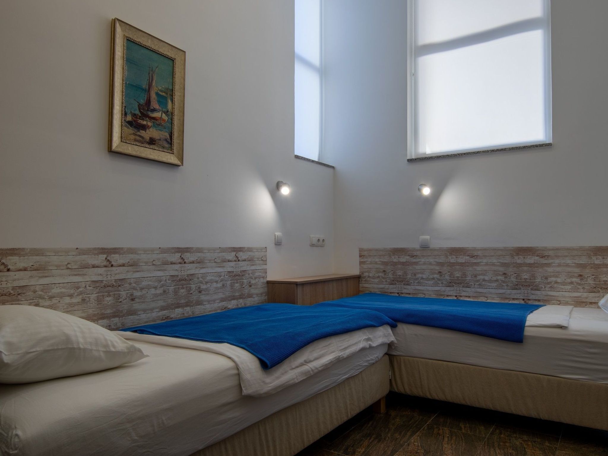 A room with two beds, a painting on the wall, and a window providing natural light.