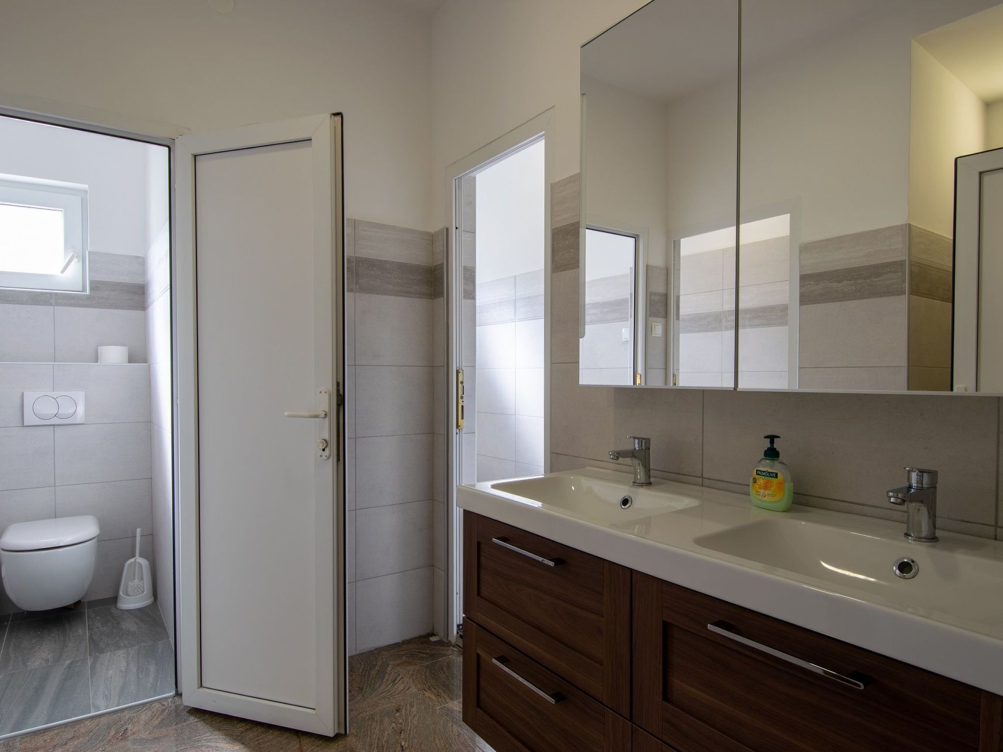 Ein modernes Badezimmer mit Toilette, Dusche und einem Waschtisch mit Spiegel und zwei Waschbecken.