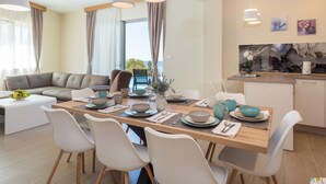 Ein modernes Wohnzimmer mit Essbereich, ausgestattet mit einer Couch, Esstisch, Stühlen und Pendelleuchten.