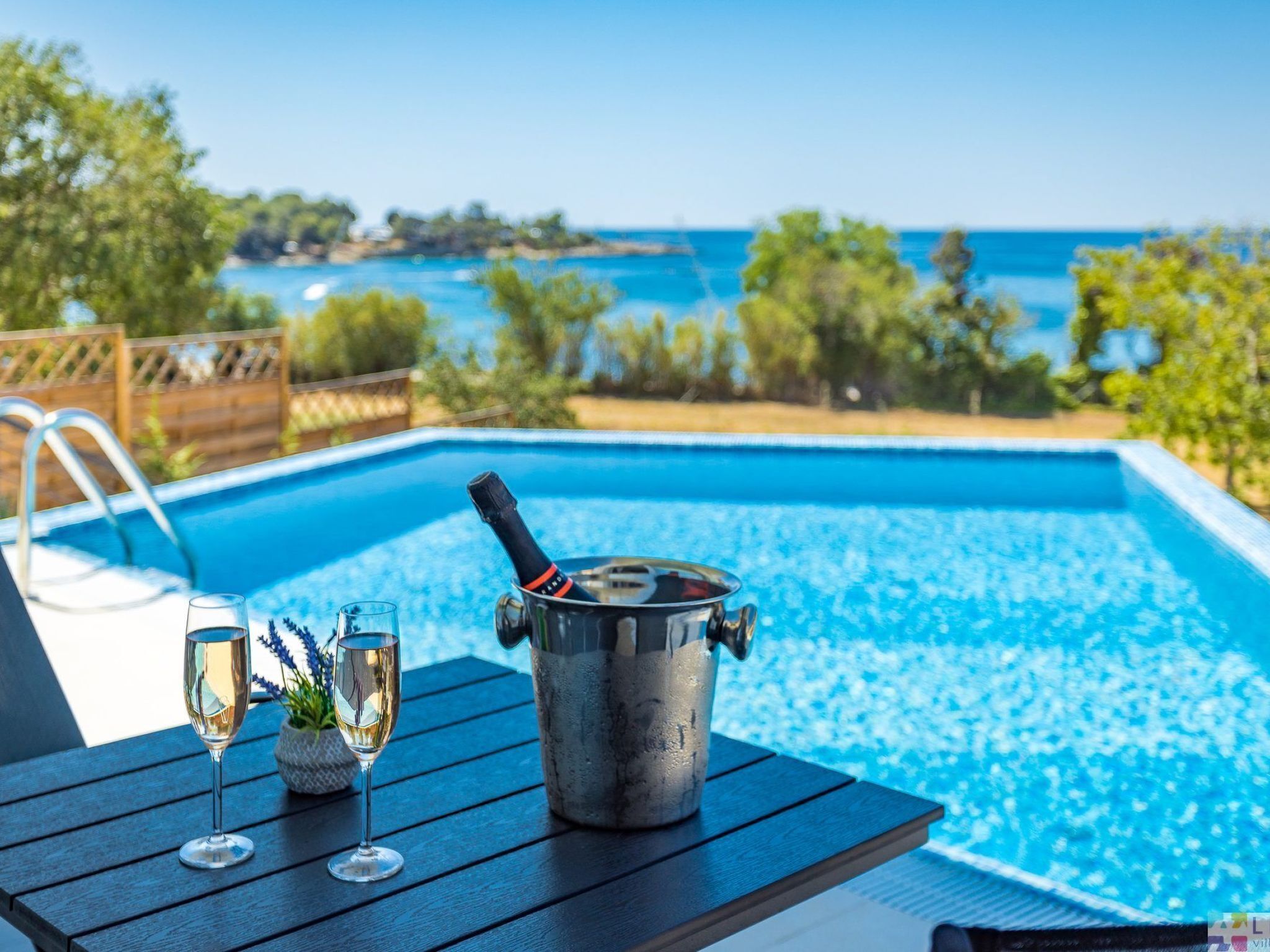En miljö vid poolen med ett bord, två champagneglas och en champagneflaska.