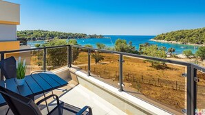 Ein Balkon mit Tisch und Stühlen, mit Blick auf eine Küstenlandschaft mit klarem, blauem Wasser und hügeligem Gelände.