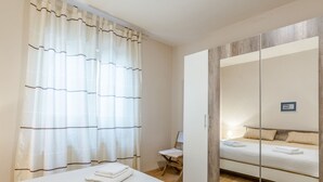 Una camera d'albergo con un letto, un armadio, uno specchio e una finestra con tende.