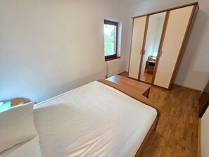 A bedroom with a bed, a wooden nightstand, a wardrobe, and a window. - Wohnung für 4-5 Personen mit Terrasse by Interhome (Crikvenica/Dramalj)