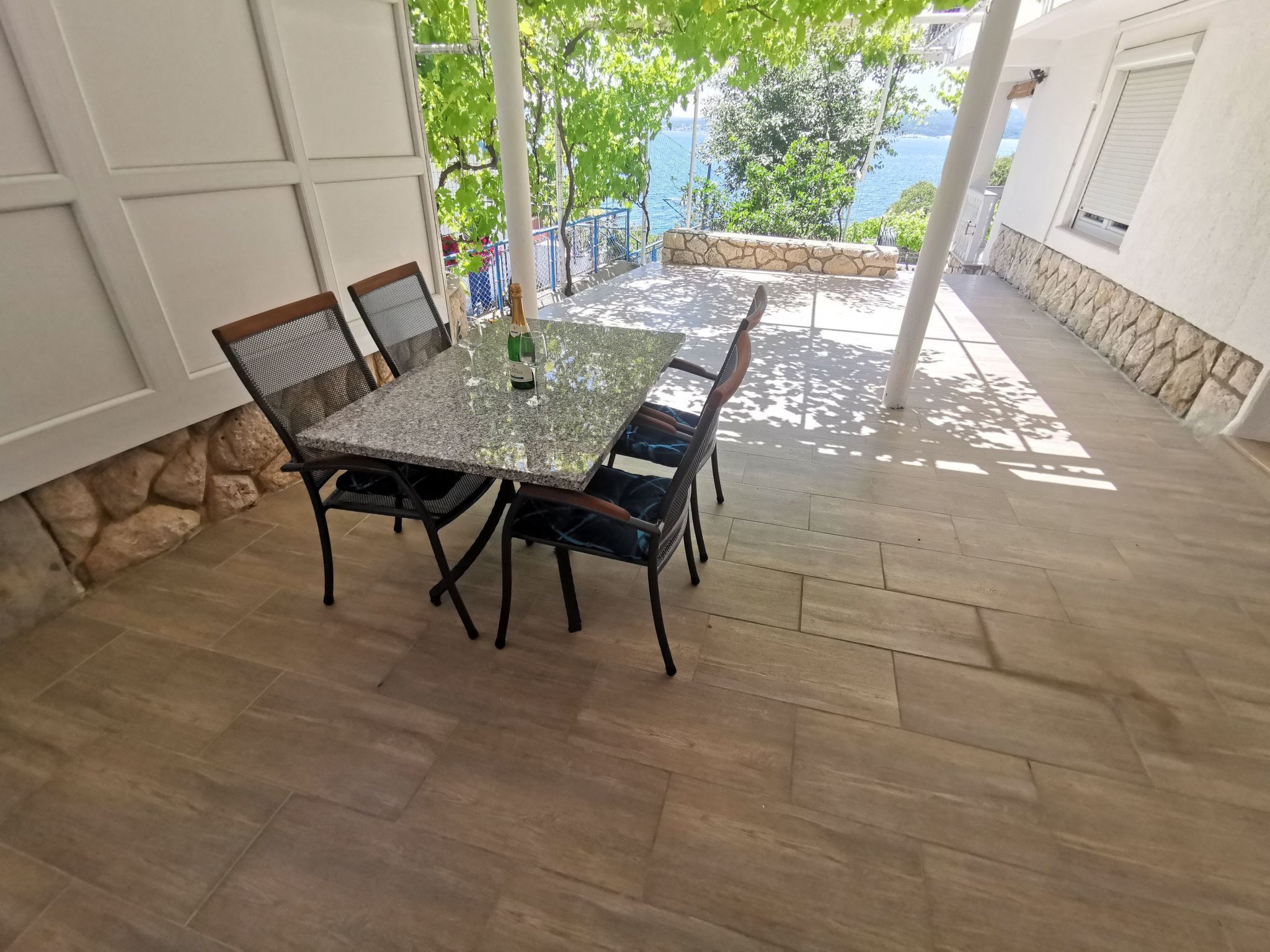An outdoor patio with a rectangular table and chairs, stone walls, and a view of the sea.