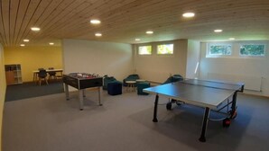 Ein Zimmer mit Tischtennisplatte, Kicker und einer kleinen Sitzecke mit Sesseln und Hocker.