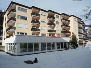A multi-story hotel with balconies, a covered entrance, and a snow-covered ground. - Relaxing Holidays by Interhome (Scuol)