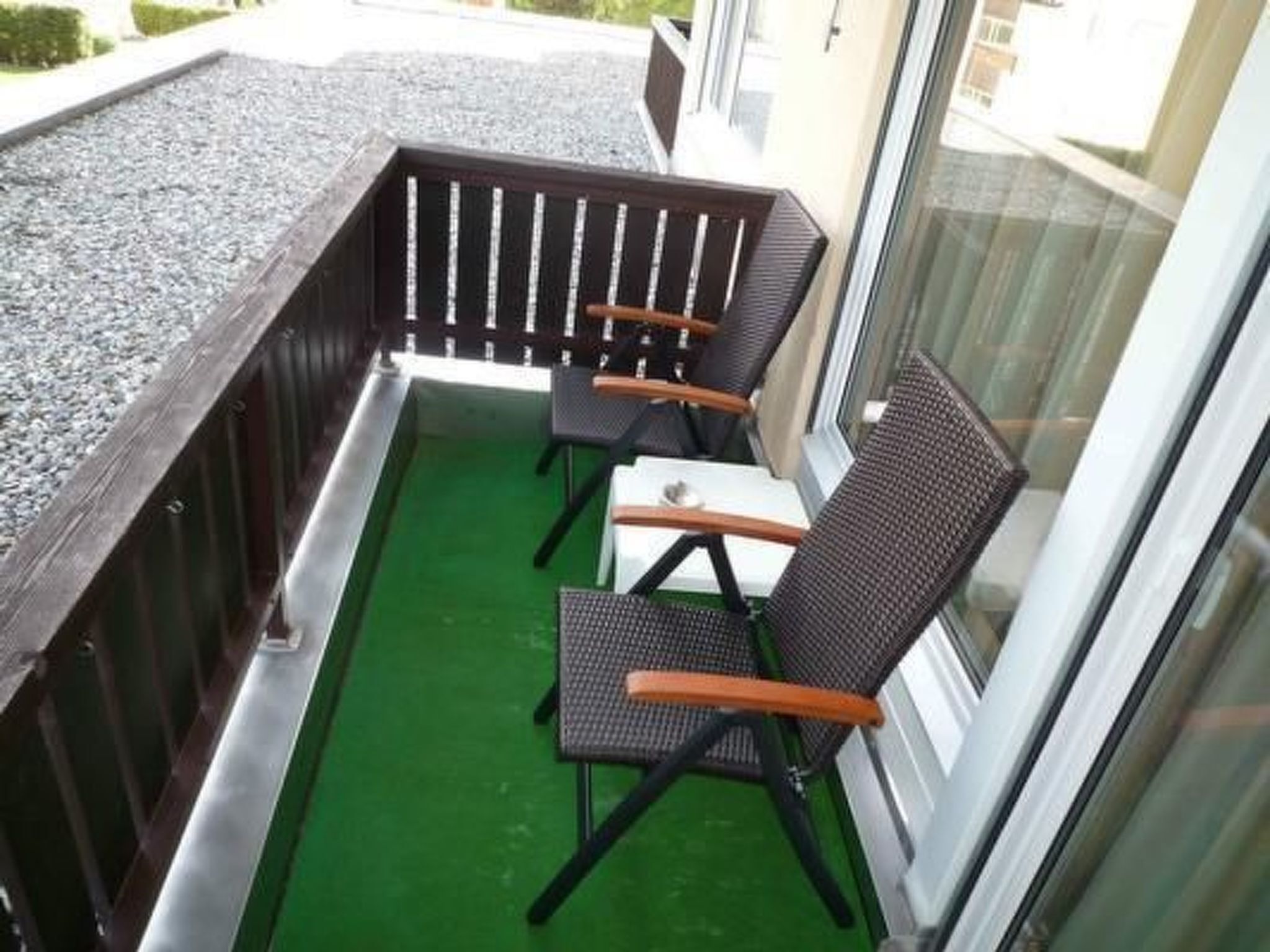 Ein kleiner Balkon mit zwei Stühlen und einem Tisch, umgeben von einem Holgitter und einer Glastür.