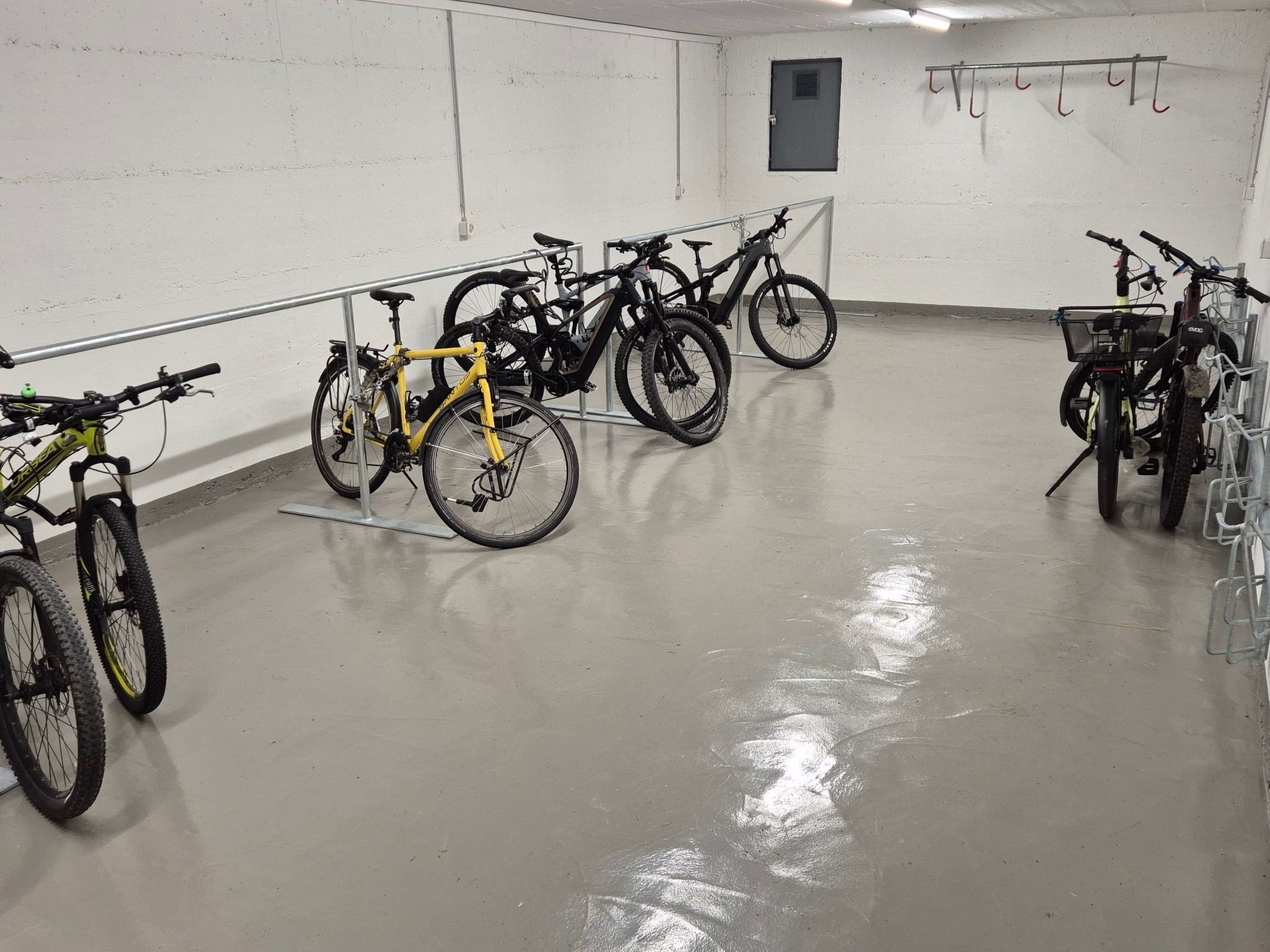 Un espace de stationnement pour vélos comprenant plusieurs vélos, une porte et un porte-vélos fixé au mur.