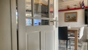 A dining area with a table and chairs, a painting on the wall, and a window with a view of the outside. - Ruhiges Ferienhaus mit großer offener Küche by Interhome (Anjum)