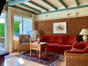 Un salon avec un canapé rouge, un fauteuil en osier, une table basse en bois et un tapis à motifs.