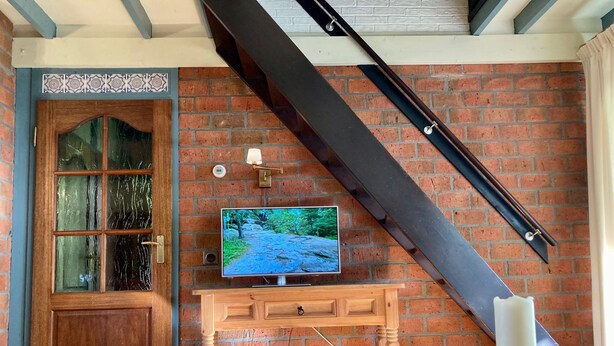A room with a wooden door, a television on a wooden console, a brick wall, and a staircase. - haus am Deich! by Interhome (Anjum)