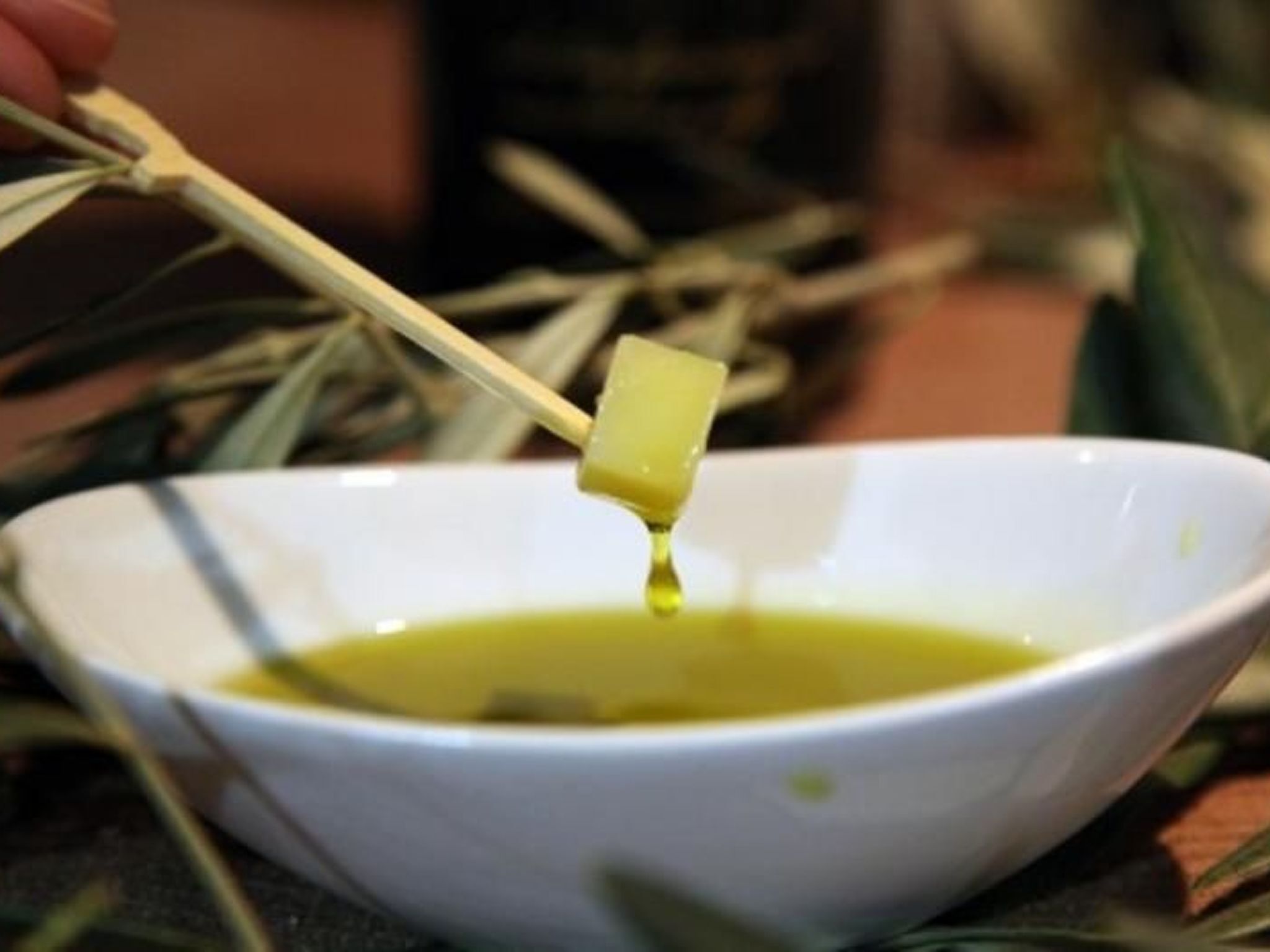 A bowl of olive oil with a chopstick holding a piece of bread.