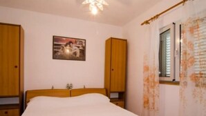 Een slaapkamer met een houten bed, nachtkastje, kledingkast en een raam met gordijnen.