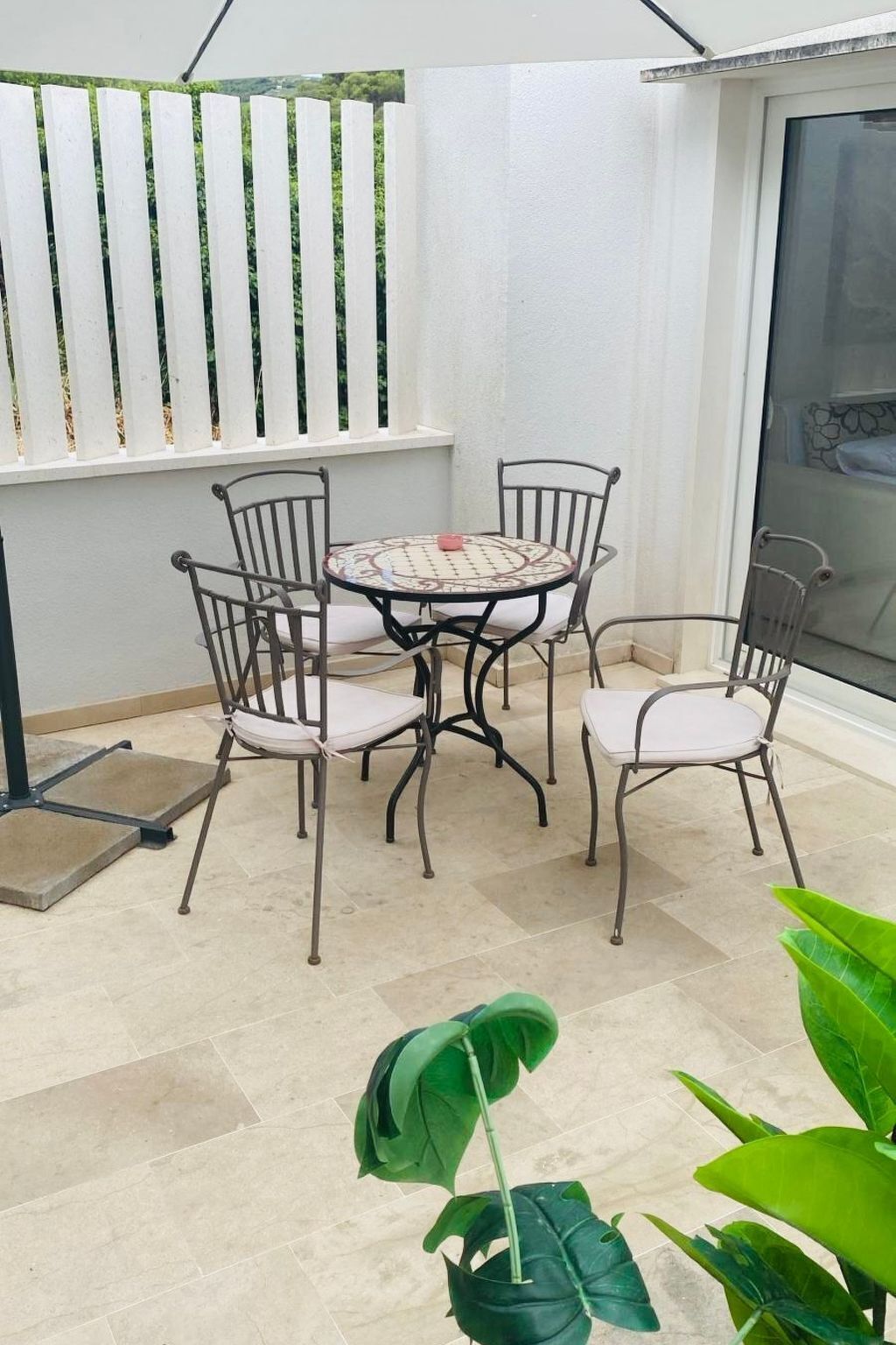 Une terrasse avec une table ronde et quatre chaises, une clôture blanche et une porte-fenêtre coulissante.