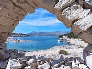 A stone archway framing a coastal view with clear blue water, rocky shore, and distant mountains. - Wohnung in Povlja mit privatem Parkplatz by Interhome (Brač/Povlja)