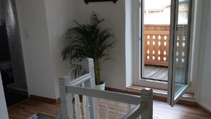 A staircase with white balusters leading to a landing, a potted plant, and a door leading to an outdoor area with a wooden deck.