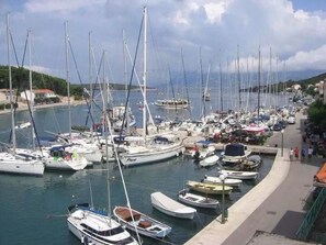 Un puerto deportivo con varias embarcaciones amarradas, un paseo marítimo y edificios al fondo.