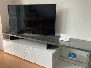 Un televisor de pantalla plana sobre un mueble de entretenimiento moderno con un estante de vidrio y un cartel que muestra la información de la red WiFi y la contraseña.