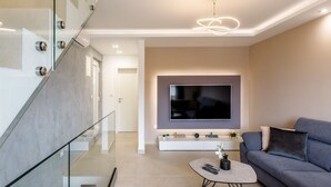 A modern living room with a flat-screen TV mounted on the wall, a grey sofa, a coffee table, and a glass staircase. - "Villa Tango" by Interhome (Trogir/Okrug Donji)