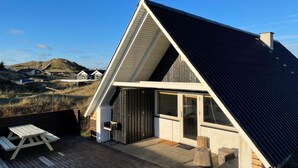 Una casa moderna con techo inclinado, ventanas grandes y un área de terraza.