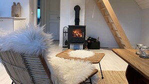 Una habitación acogedora con una butaca blanca y mullida, una mesa de mimbre y una estufa de leña.