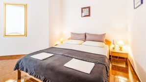 Et hotelværelse med en seng, sengeborde med lamper, et billede i ramme på væggen og en klimaanlæg.