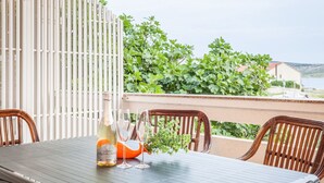 Et bord med en flaske og glas, træstole, samt udsigt til grøn natur og bygninger.