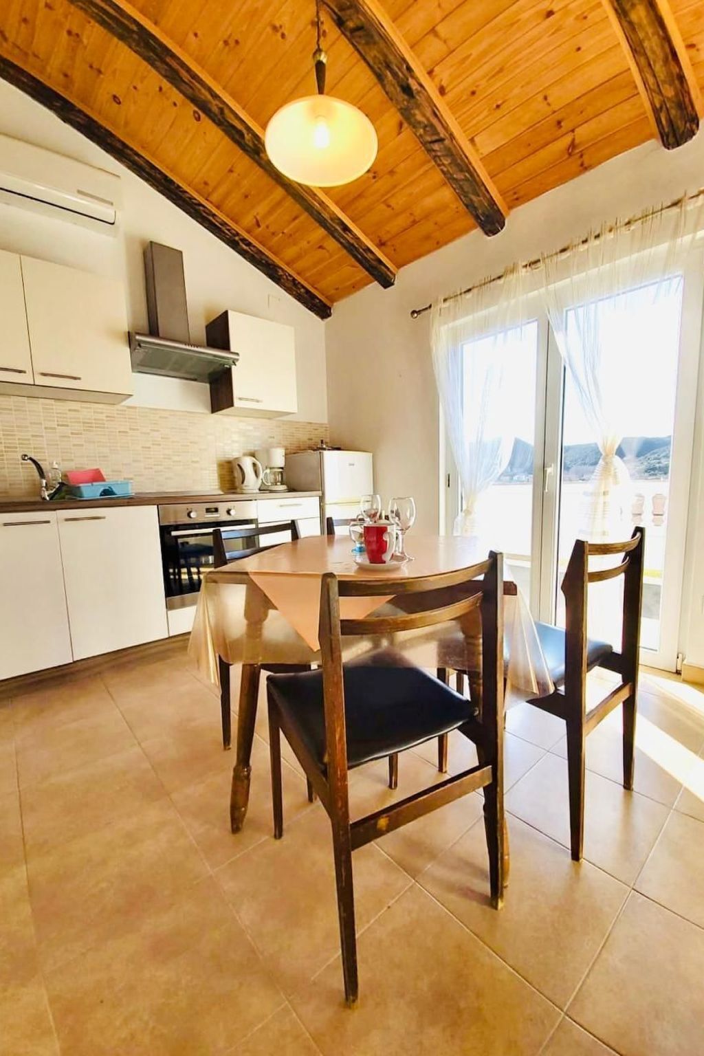 A kitchen with a dining table and chairs, a view of a body of water, and a wooden ceiling.