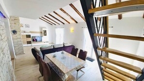 A modern living room with a dining table, sofas, and a kitchen in the background. - Apartment Karlo auf zwei Wohnebenen, mit Meerblick by Interhome (Rab/Supetarska Draga)