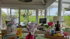 Et værelse med et stort vindue, et fjernsyn, en pink vase med blomster og forskellige genstande på et bord.