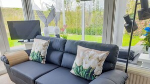 En mørk lædersofa med hvide tulipanpuder, et fladskærms-tv og en lampe.